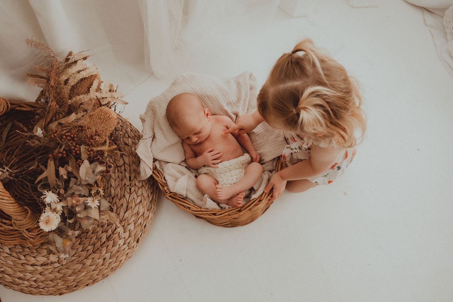 Newborn baby sleeping peacefully on lace blanket with natural woven basket decor.