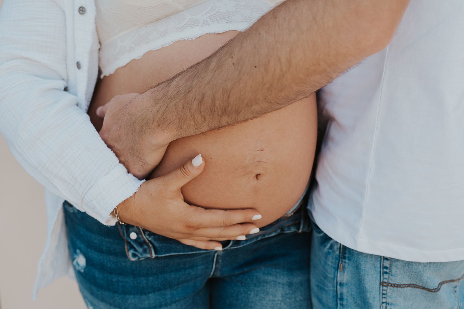 Close-up photo of hands cradling a pregnant belly in denim, studio maternity photography in Michigan.