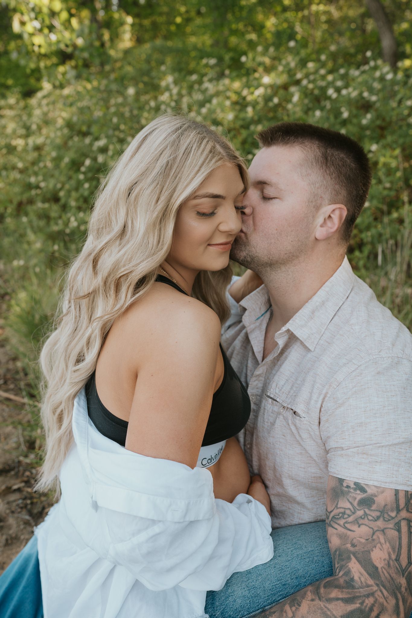 Intimate couple photoshoot in a wooded setting with romantic poses and natural lighting.
