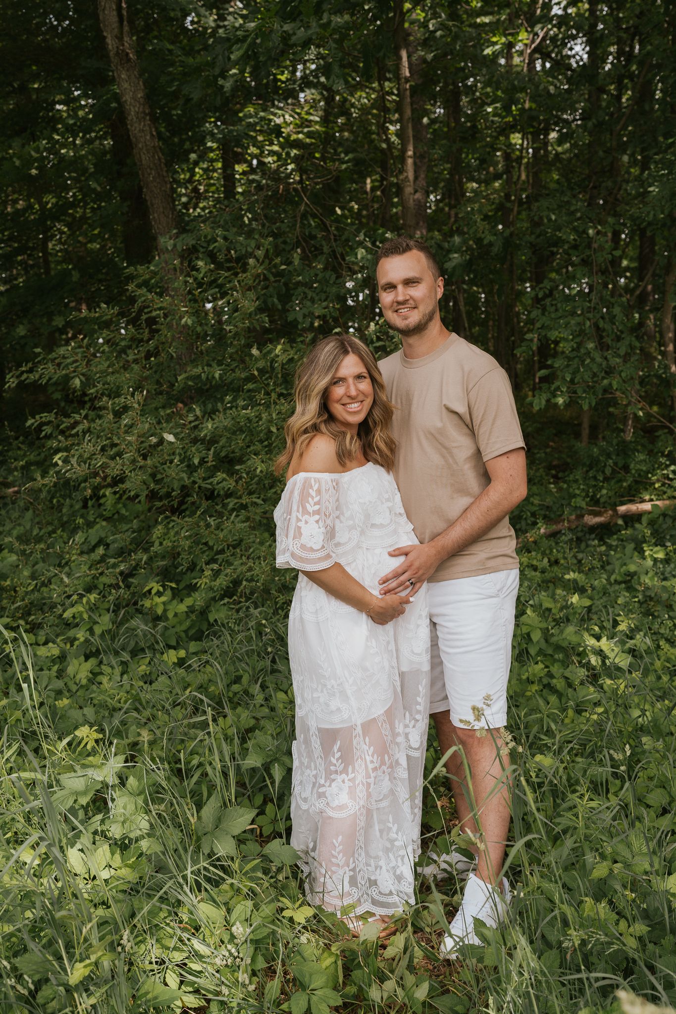 Michigan couple in white outfits pose for romantic photos in lush green forest setting.