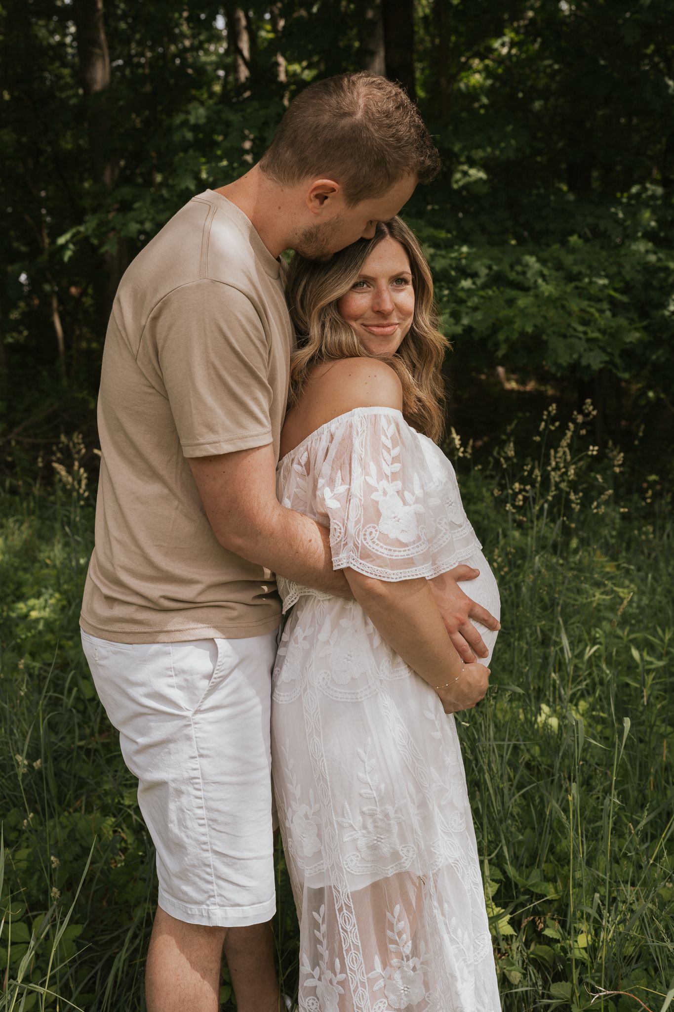 Intimate maternity photos with couple in white attire against forest backdrop in Jackson Michigan.