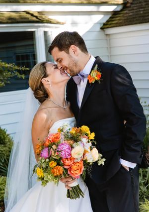Romantic couple poses with vibrant colorful wedding bouquet against white building. St Michael's Maryland