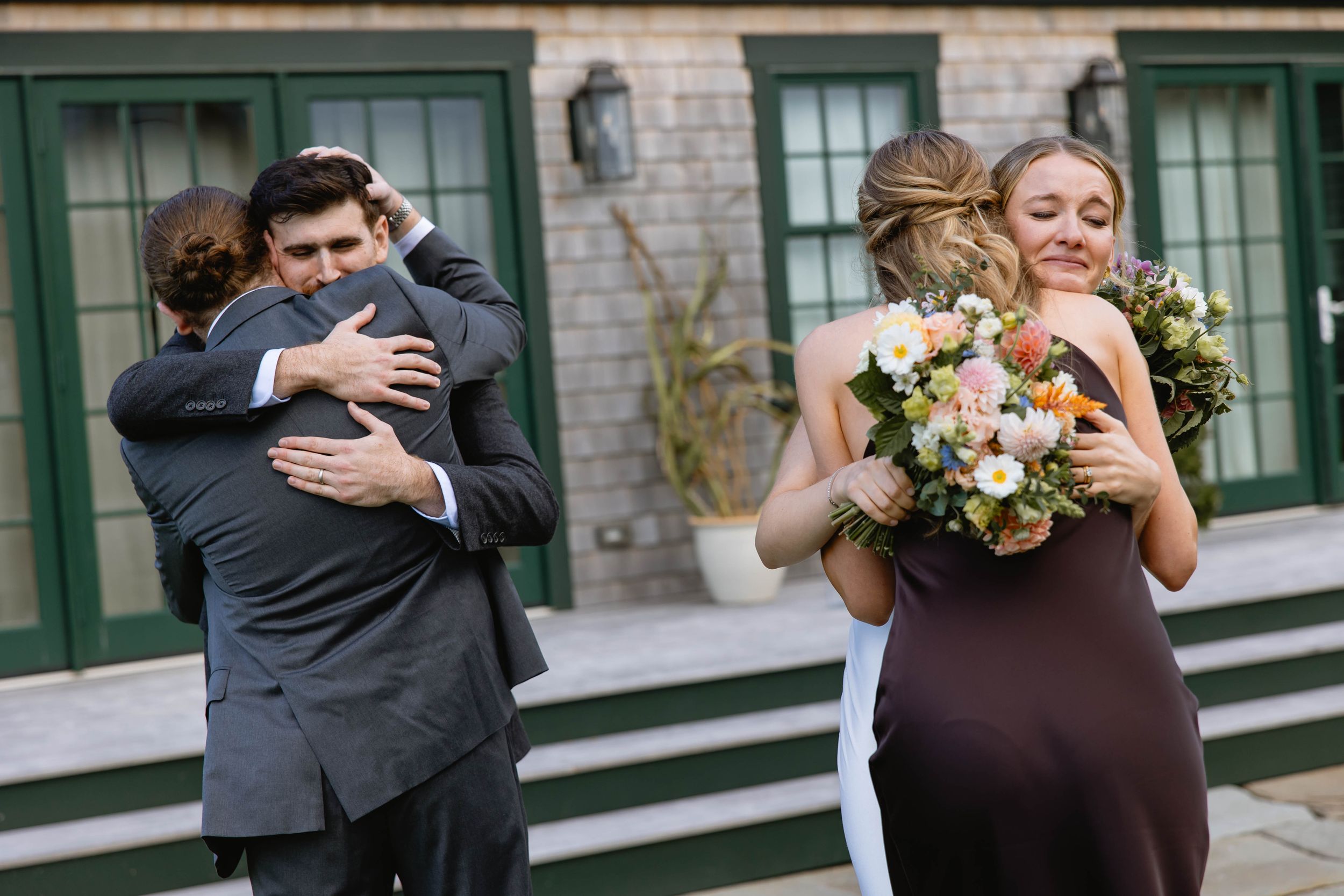 Wedding party exchanging warm embraces outside a historic stone building.