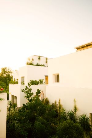 Modern white Mediterranean villa with tropical landscaping and palm trees against a warm sunset sky.