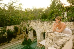 A couple shares a romantic moment on stone ruins surrounded by lush greenery and sunlight.