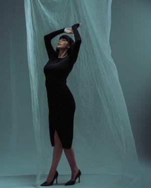 Silhouette of a graceful figure in a black dress striking a dramatic pose against ethereal teal fabric backdrop.