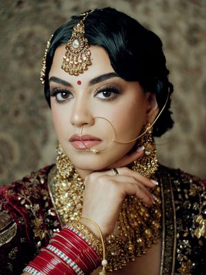 Traditional Indian bridal makeup with ornate gold jewelry and red bangles showcases elegant cultural wedding fashion.