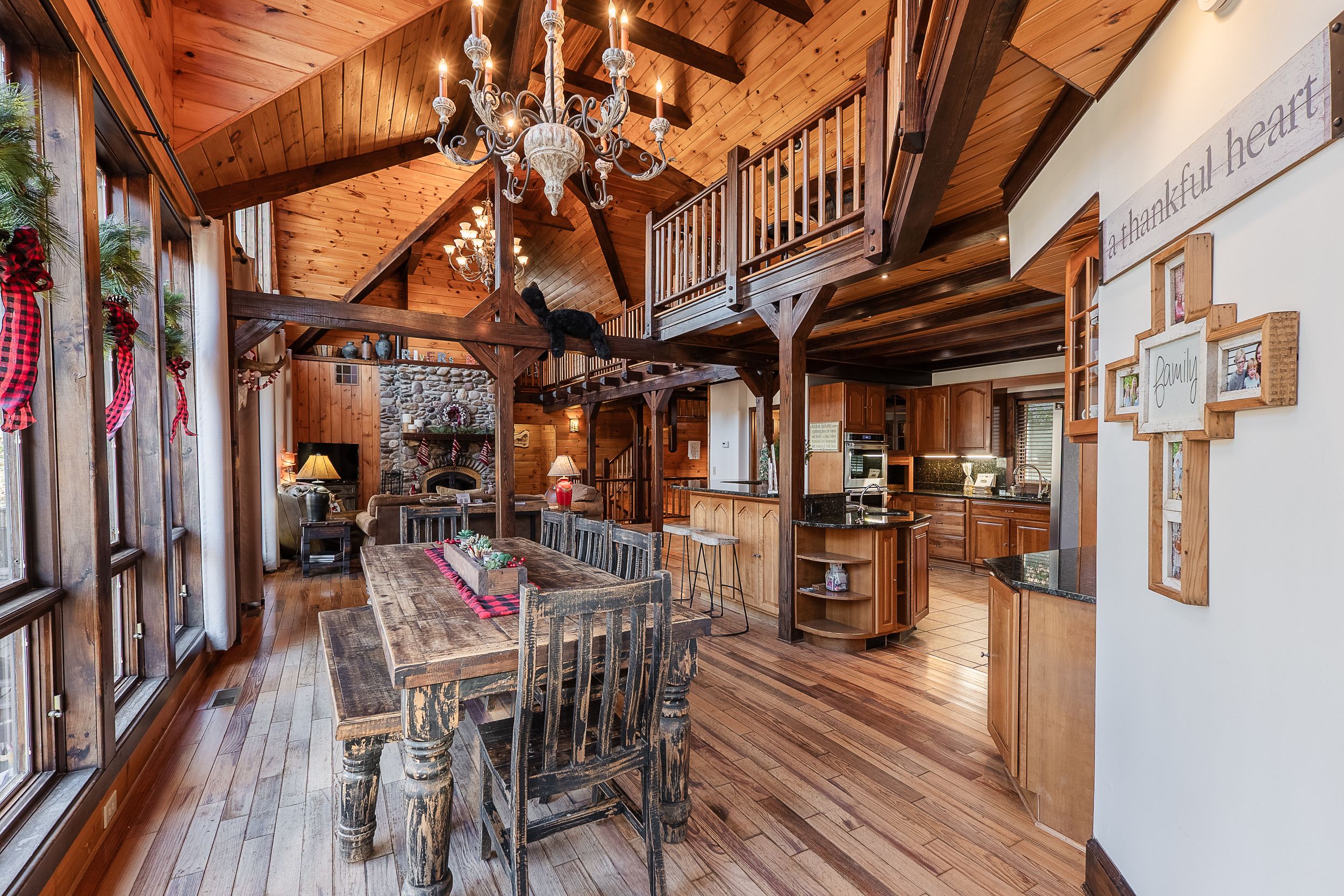 Rustic mountain cabin interior with wooden beams, chandelier, and long dining table in an open-concept living space.