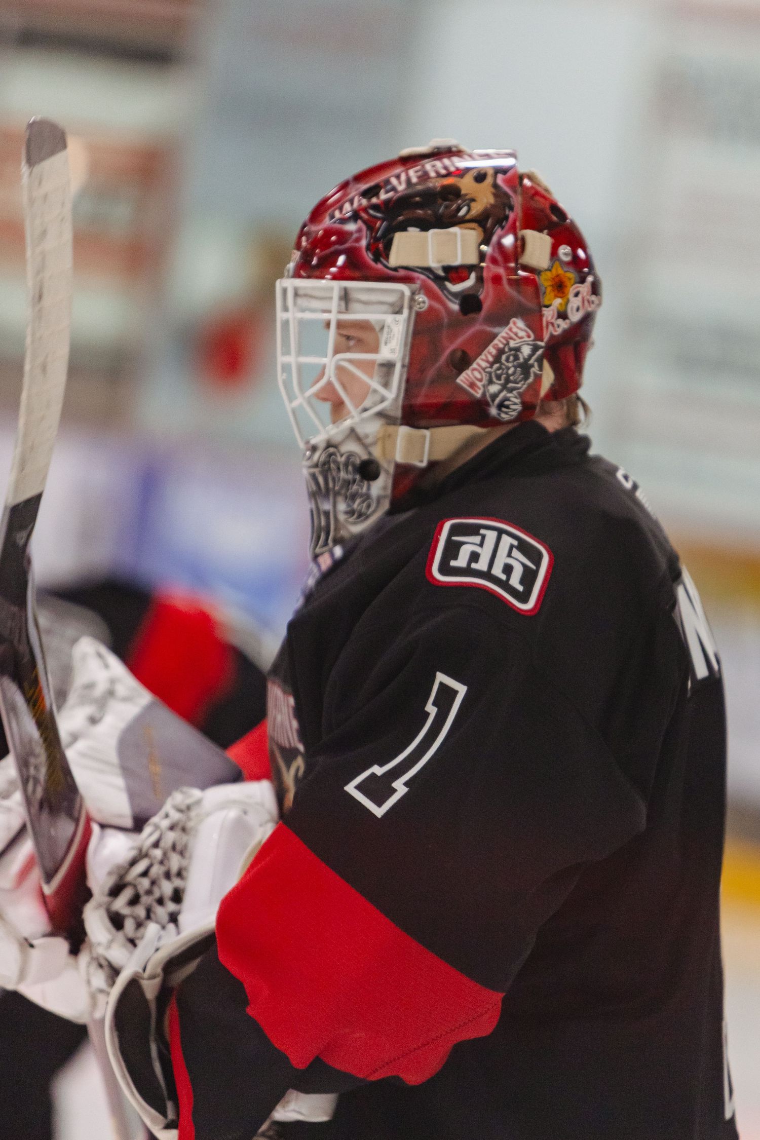 A hockey team's goalie side profile holding his hockey stick.
