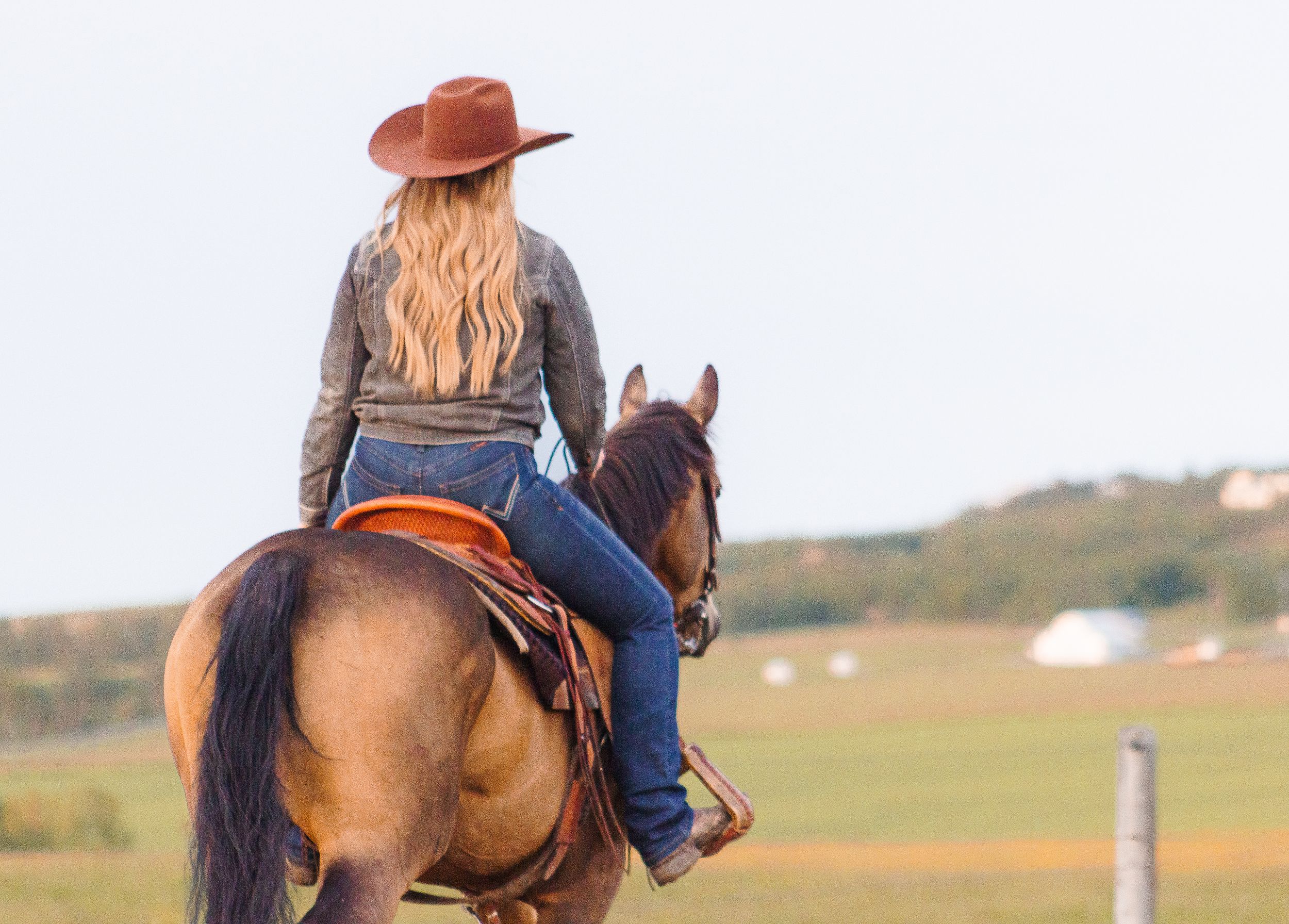A western styled woman rides her brown horse away from the camera.