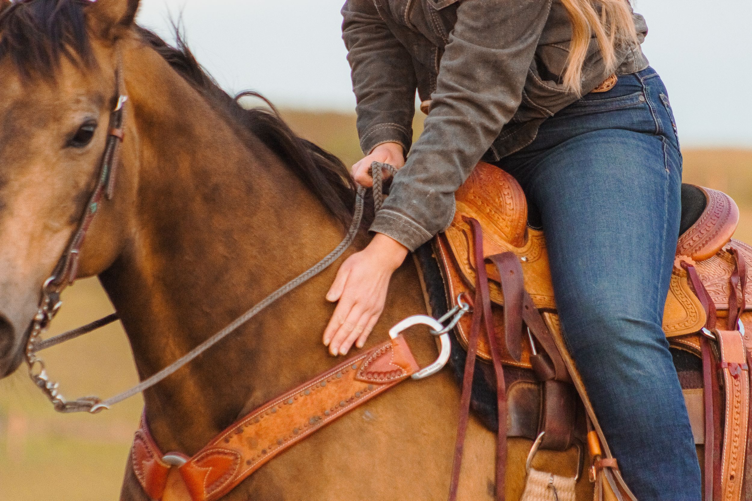 A picture of a woman in a saddle leaning down to pet her horse.