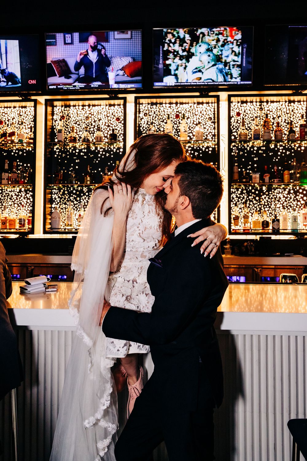 Wedding, bride and groom sitting on bar top touching foreheads and kissing in the twinkling glow by Photogenic Fox Photography