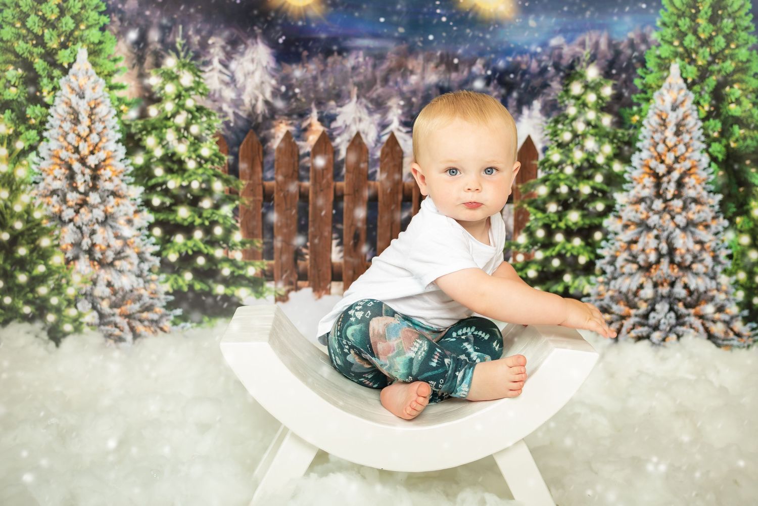 Little girl and boy sat on a mini bench in a Christmas scene, snow on the floor and candy canes in the background