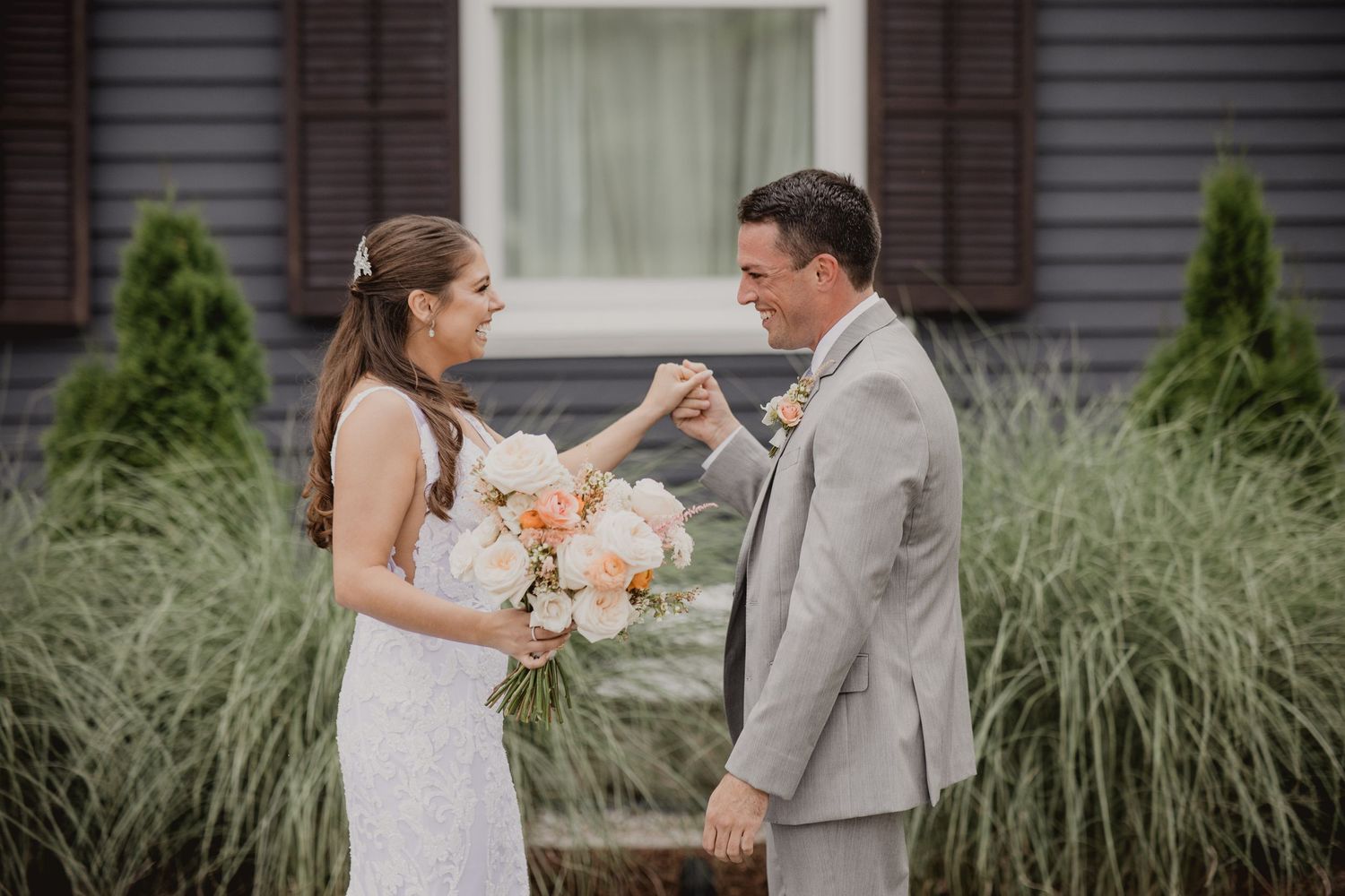 Elegant wedding portraits taken against a grey house with decorative shutters and ornamental grasses.