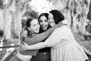 Three friends sharing a joyful group hug outdoors against a backdrop of trees.