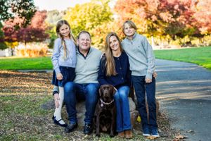 Happy family with two children and a chocolate lab dog posing together outdoors during autumn.