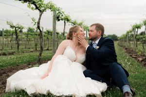 Bride and groom sitting together in a lush vineyard, sharing a romantic moment in wedding attire.