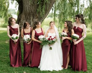 Bride in white gown poses with five bridesmaids in burgundy dresses holding red and white bouquets.