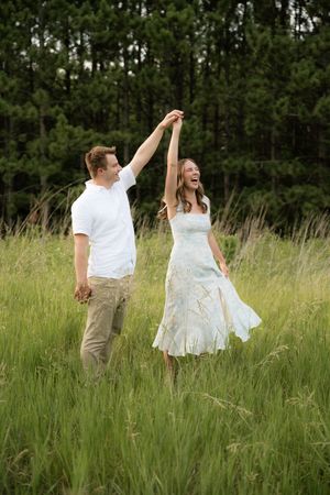 A joyful couple dancing in a lush green meadow, man in white shirt twirling woman in flowing light dress.