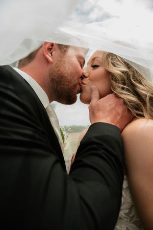 Bride and groom sharing a romantic kiss under a flowing white veil on their wedding day.