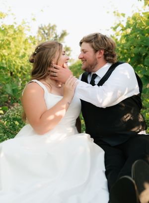 Bride and groom share a tender moment in a vineyard, groom gently cupping brides face as they smile at each other.