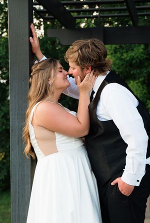 A bride and groom share a romantic almost-kiss under a pergola outdoors at their wedding ceremony.