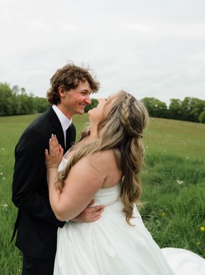Newlywed couple shares romantic moment in green meadow, bride in white gown and groom in black tuxedo.