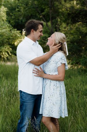Couple in casual white outfits share a romantic moment in a lush green meadow, man tenderly holding womans face.