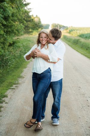 A happy couple embraces on a scenic dirt road lined with trees during an outdoor engagement photo session.