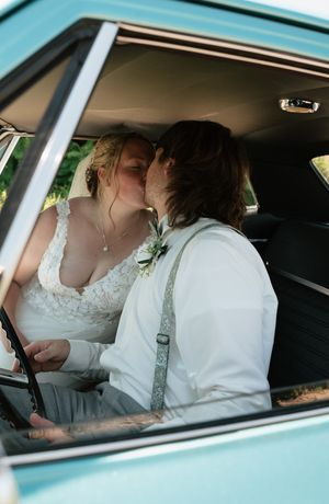 Bride and groom sharing a kiss inside a vintage teal car on their wedding day.