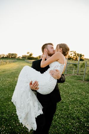 A romantic dip kiss between newlyweds in formal attire at sunset in a vineyard setting.