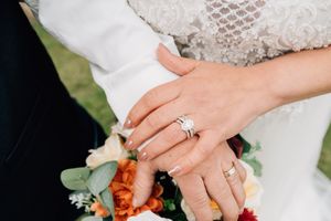 Close-up of newlyweds' hands with wedding rings resting on a colorful floral bouquet.