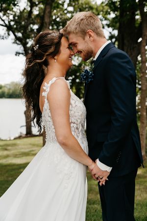 A couple shares an intimate moment during their outdoor wedding photoshoot near a lake with trees in the background.