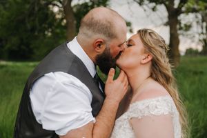 A romantic moment between newlyweds sharing a kiss in a lush green outdoor setting.