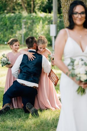 Wedding party relaxes on grassy lawn wearing pink and navy attire during outdoor photo session.