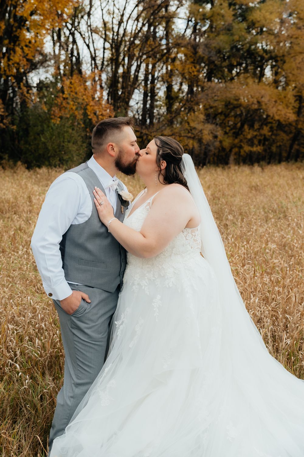 Romantic autumn wedding scene with couple kissing in a golden field of tall grass during fall season.