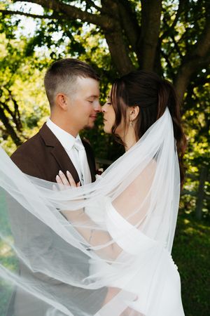 A romantic wedding photo series with a flowing white veil caught in the breeze against a green forest backdrop.