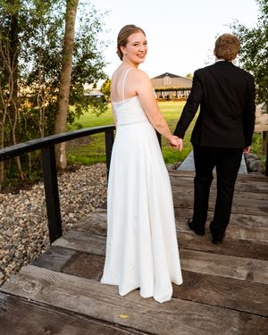 Couple in formal wedding attire walks along a rustic wooden deck on their special day.