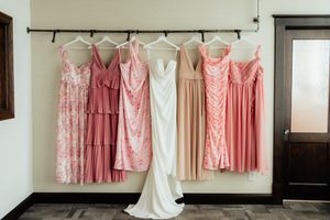 A row of pink and white bridesmaid dresses hanging on a clothing rack against a white wall.