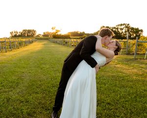 Romantic wedding couple embraces in a golden sunset field with rolling hills in the background.