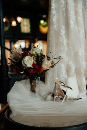 Wedding dress hem with bridal bouquet and shoes arranged in soft lighting with romantic details.