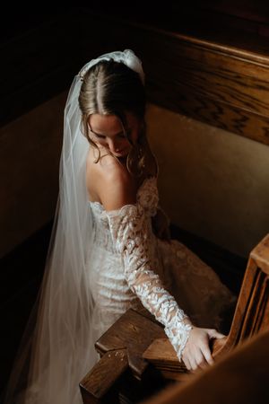 Dramatic moody lighting illuminates a wedding dress with delicate lace details and flowing veil in a rustic wooden setting.