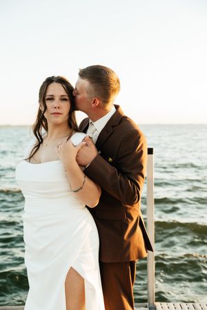 Seaside wedding portraits with couple embracing against ocean backdrop at sunset.