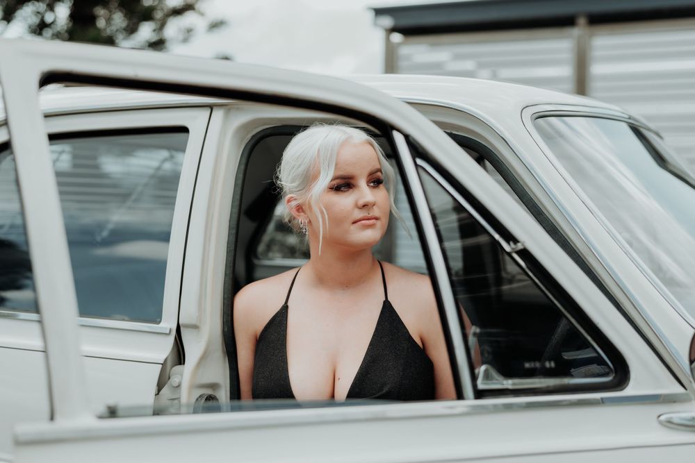 Someone in formal attire sitting in the driver's seat of a vintage white car.