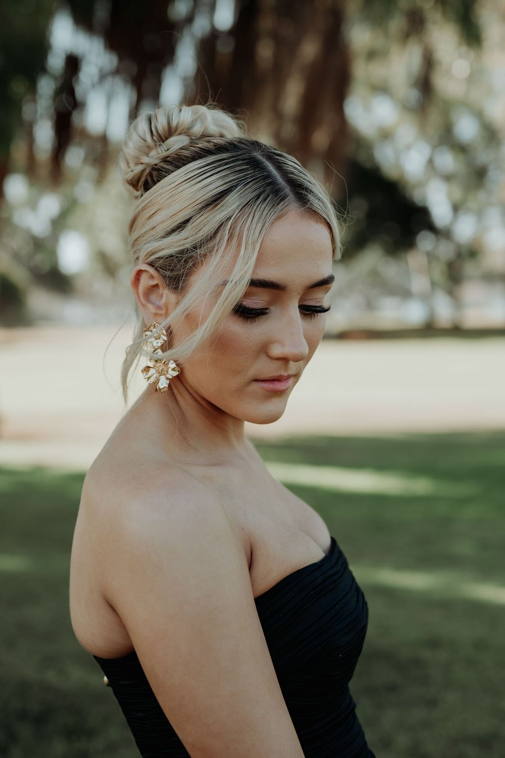 Portrait in black strapless dress with delicate earrings in outdoor garden setting.