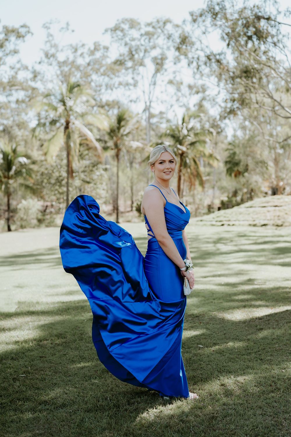 A flowing royal blue dress twirls in the sunlight on a grassy lawn with palm trees at gladstone garden.