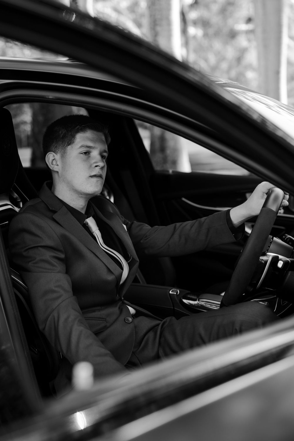 Black and white portrait of someone in formal attire sitting in a luxury car.