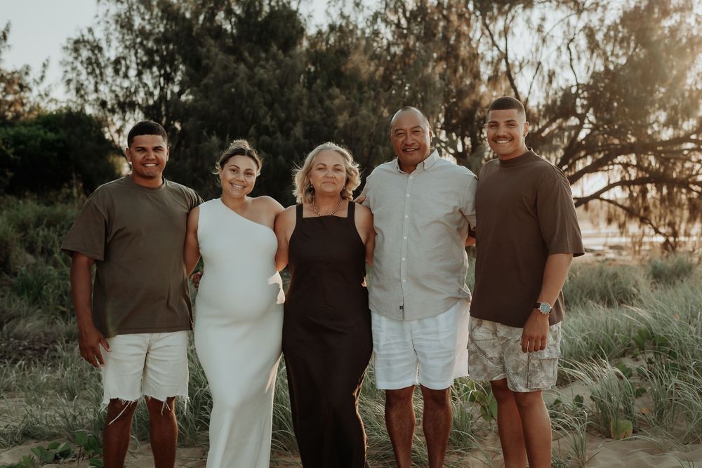 Family standing together on a gladstone beach with coastal vegetation.