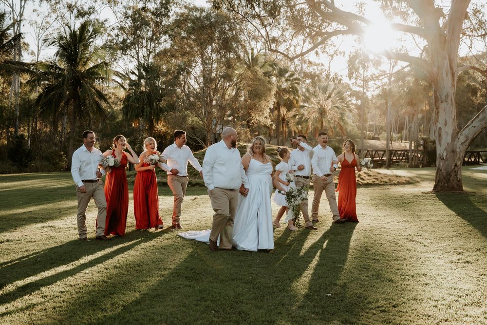 Wedding celebration with guests in red dresses and white attire dancing in sunlit toondoon botanic gardens.