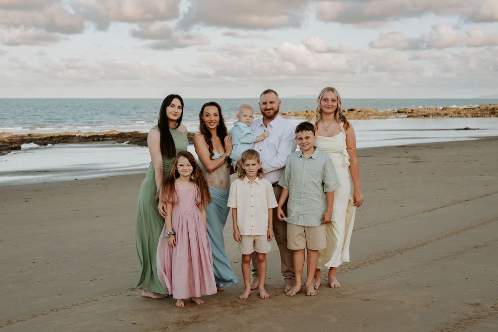 Group portrait of family members wearing coordinated pastel outfits on gladstone beach at sunset.